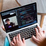 Person coding on a laptop during a video conference, showcasing remote work.